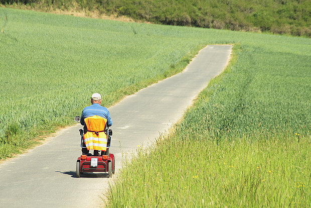 Rollstuhlfahrer auf einsamen Fahrradweg im Grünen