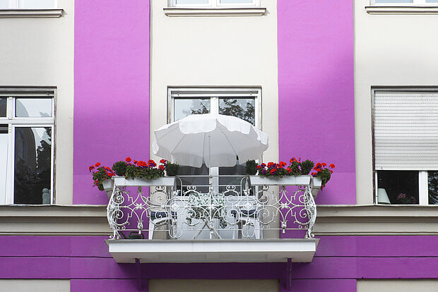 weißer Balkon vor einer violetten Hausfassade