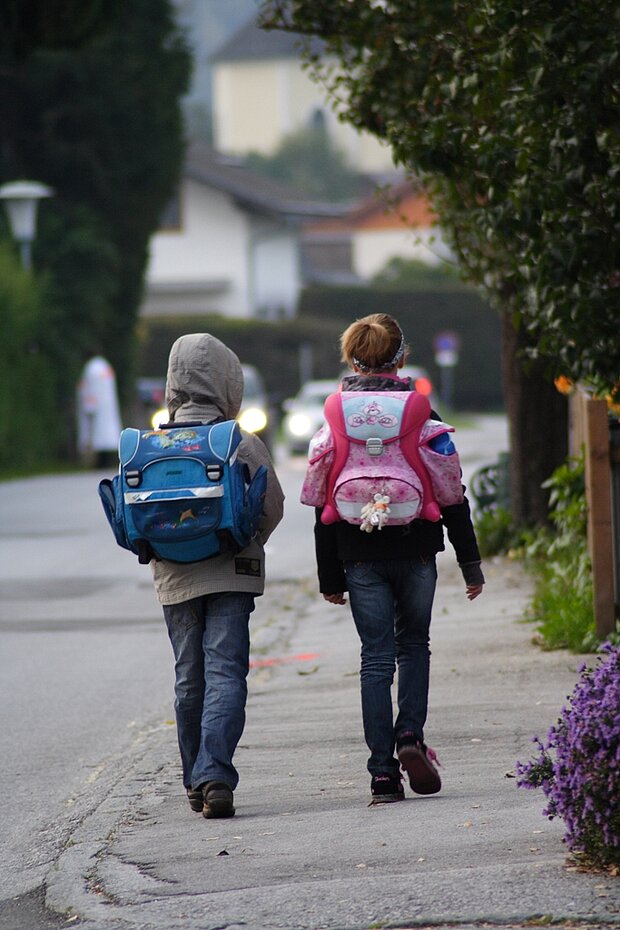 Zwei Schulkinder mit Schulranzen laufen eine Straße entlang