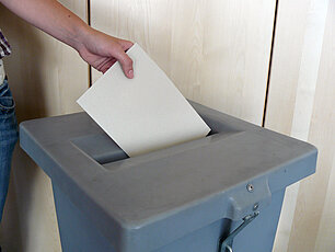 Person wirft Stimmzettel in die Wahlurne