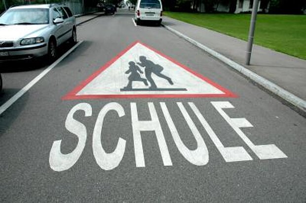 Straße mit einer Aufschrift Schule und einem Warnsymbol mit Schulkindern