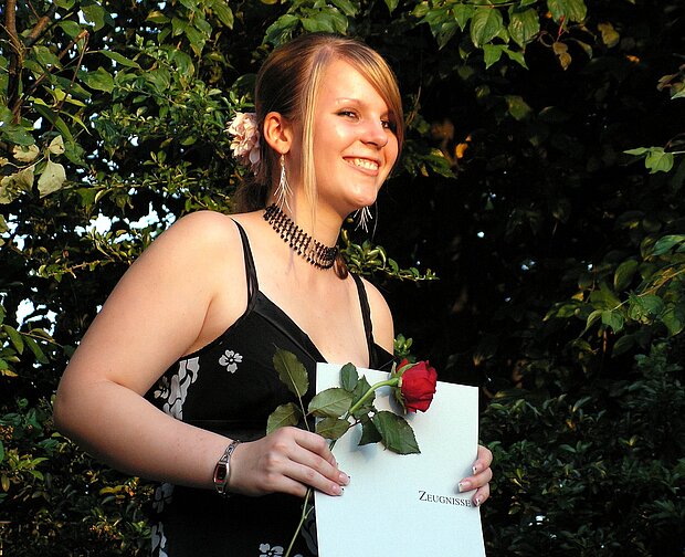 glückliche junge Frau mit Zeugnis und Rose in der Hand