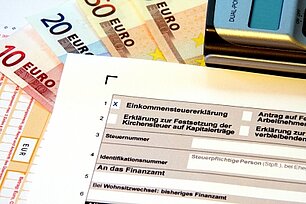Einkommensteuerbescheid liegt auf Geldscheinen