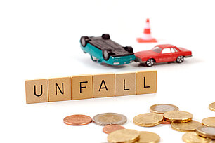 Spielzeugautos im simulierten Unfall, Geldstück und Scrabble Wort "Unfall"